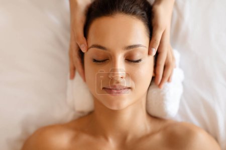 Friedliche Europäerin, die eine heilende Kopfmassage von einer professionellen Masseurin im modernen Luxus-Wellnessbereich bekommt, Blick von oben. Nahaufnahme einer Frau, die während einer Massage Entspannung genießt