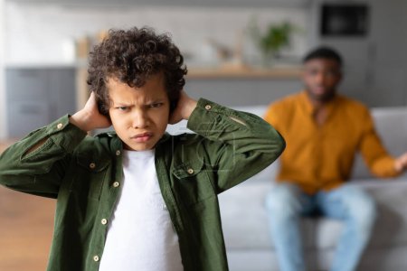 Nahaufnahme eines beunruhigten Jungen mit genervtem Gesichtsausdruck im Vordergrund, bei dem streitende Eltern aus dem Fokus geraten