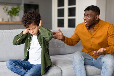 Foto de Un niño se cubre los oídos mientras su padre grita frustrado, representando un tenso escenario familiar. - Imagen libre de derechos