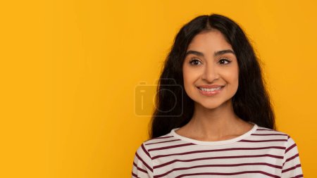 Photo for A calm and collected young woman in a striped shirt stands against a yellow background, evoking a sense of tranquility - Royalty Free Image
