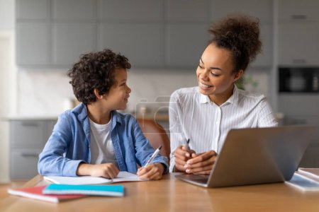Madre ayuda a su hijo con los estudios delante de una computadora portátil en un ambiente cálido hogar
