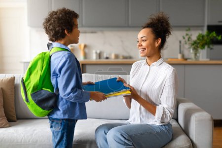 Son receiving notebooks and school supplies from mother in a home environment