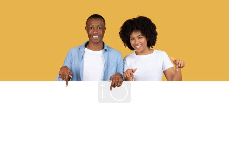 Téléchargez les photos : Un heureux couple afro-américain millénaire pointe vers la caméra avec des sourires brillants, portant des vêtements décontractés sur un fond jaune vif, suggérant une sélection ou une promotion - en image libre de droit