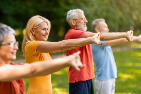 Photo for Group of happy seniors doing stretching exercises while training outdoors, smiling elderly men and women extending arms forward, practicing yoga together, enjoying active lifestyle on retirement - Royalty Free Image