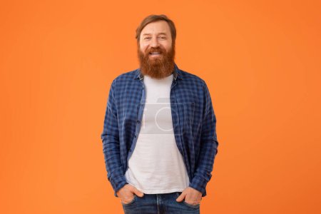 Photo for Positive European Man With Red Hair And Beard Posing Holding Hands In Pockets Standing Over Orange Studio Background. Cheerful Redhaired Guy Smiling To Camera Expressing Positive Emotions - Royalty Free Image