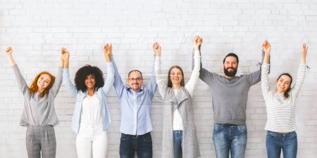 Photo for Group of successful friendly people raising connected hands, white brick wall background - Royalty Free Image
