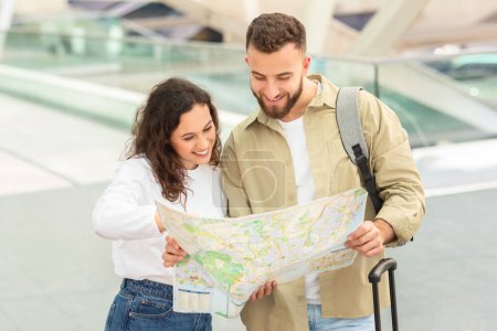 Photo for Smiling young couple looking at map together while standing in airport terminal, happy man and woman checking route, planning their travel itinerary, feeling excited for the adventure ahead - Royalty Free Image