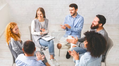 Photo for Friendly therapy group members applauding to young womans progress in rehabilitation, sitting together in trust circle and clapping hands - Royalty Free Image