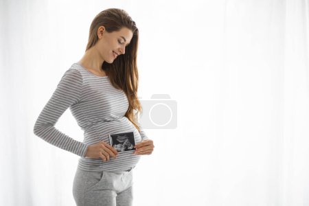 Foto de Una futura madre echa un vistazo a una foto de ultrasonido, una conexión especial con la vida que crece dentro - Imagen libre de derechos