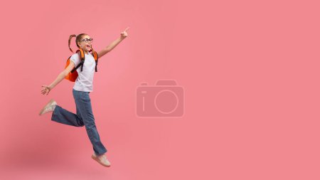 Téléchargez les photos : Jeune fille excitée et heureuse bondissant dans l'air, pointant vers le haut sur un fond rose - en image libre de droit