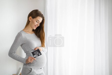 Cheerful expectant mother holding an ultrasound photo, sharing a special moment