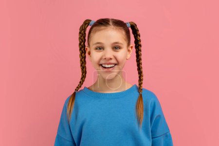 Ein fröhliches junges Mädchen mit langen geflochtenen Haaren lächelt breit vor rosa Hintergrund