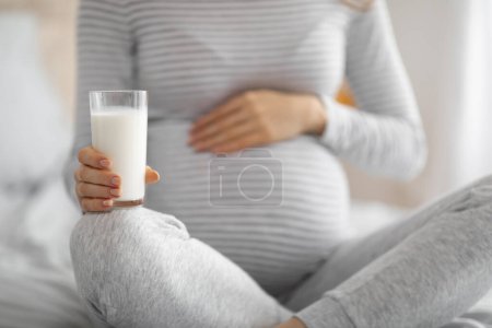 Foto de Una imagen pacífica de una mujer embarazada acunando su vientre mientras sostiene un vaso de leche nutritiva, que representa la salud y la atención prenatal - Imagen libre de derechos