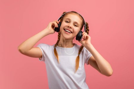 Téléchargez les photos : Une fille heureuse écoute de la musique avec de gros écouteurs et danse sur un fond rose - en image libre de droit
