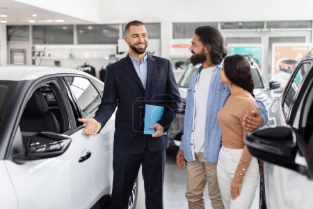 Friendly car salesman explains car features to an interested indian couple in a car dealership
