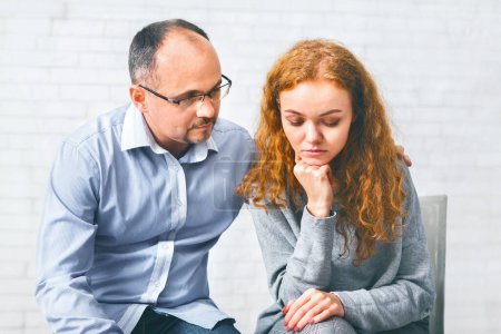 Caring husband supporting his depressed wife at marriage therapy session in counselors office, encouraging her to share problems