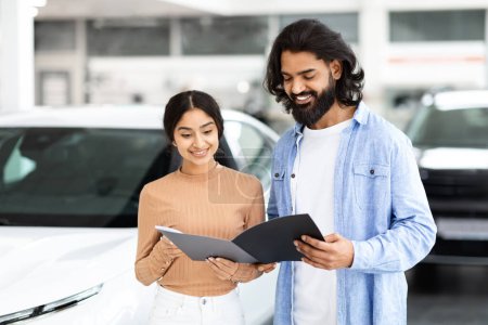 Photo for A young indian couple is focused on reviewing a car brochure together in a vehicle showroom - Royalty Free Image