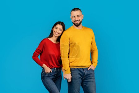 Photo for Cheerful man and woman in bright casual attire smiling and standing close together, happy young couple posing against vivid blue background in studio setting, smiling at camera, copy space - Royalty Free Image