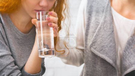Psychotherapist comforting depressed woman domestic violence victim, giving her glass of water to calm on therapy session
