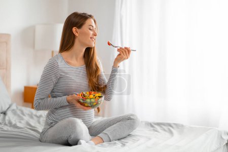 Foto de Una mujer embarazada saborea una ensalada fresca, destacando la importancia de una dieta saludable para las madres embarazadas - Imagen libre de derechos
