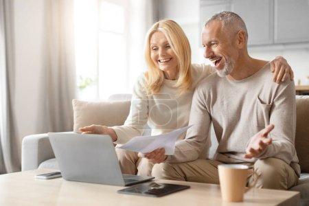 Couple d'âge mûr souriant discutant joyeusement avec des papiers et un ordinateur portable, assis sur un canapé dans une pièce lumineuse