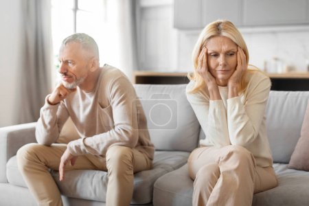 Photo for A middle-aged man and woman sit apart on a couch, seemingly lost in their own deep thoughts - Royalty Free Image