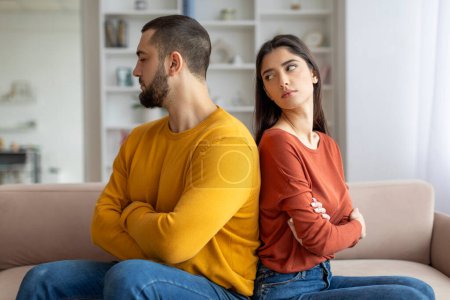 Photo for A man and woman show signs of a disagreement, sitting on a couch with arms folded, facing away - Royalty Free Image
