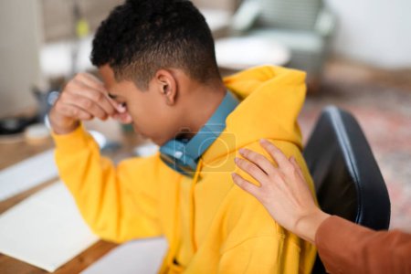 Photo for Overwhelmed teen guy feels stress during study session, takes moment of respite, with reassuring hand on his shoulder, mother comforting guy - Royalty Free Image
