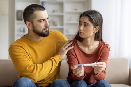 Téléchargez les photos : Le couple regarde attentivement un test de grossesse, ce qui reflète l'inquiétude et l'incertitude - en image libre de droit
