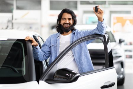 Téléchargez les photos : Homme indien souriant avec barbe debout près d'une nouvelle voiture blanche tenant des clés de voiture, peut-être à un concessionnaire - en image libre de droit