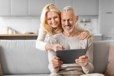 Photo for Smiling older couple enjoying content on a digital tablet, indicating a sense of sharing and engagement at home - Royalty Free Image