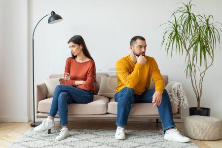 Ein Mann und eine Frau, die auf einer Couch sitzen, wirken distanziert und aufgebracht, was auf einen Konflikt hindeutet