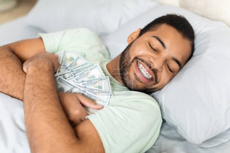 Una visión intrigante del hombre afroamericano abrazando una pila de dinero en efectivo en la cama, destacando las nociones de riqueza y éxito