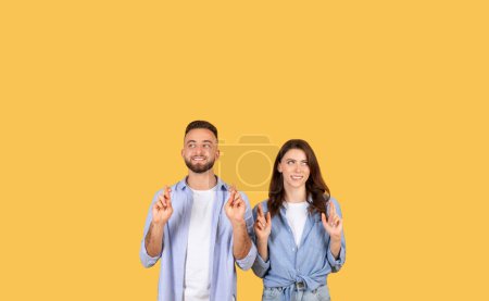 Un hombre y una mujer con expresiones esperanzadoras, cruzando los dedos para tener buena suerte