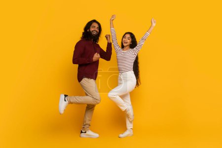 Foto de Hombre y mujer enérgicos saltan con brazos elevados y expresiones eufóricas sobre fondo amarillo - Imagen libre de derechos