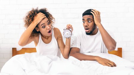 Photo for Oversleeping. Young african-american couple missed ringing of alarm clock and are late, sitting in bed, panorama, copy space - Royalty Free Image