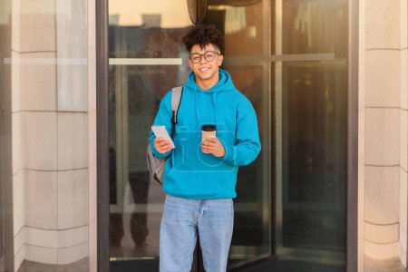 Foto de Un estudiante brasileño equipado con café y teléfono inteligente entra en un edificio de vidrio moderno - Imagen libre de derechos