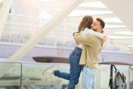 Téléchargez les photos : Un homme et une femme joyeux embrasser avec amour dans un cadre lumineux et moderne de l'aéroport comme l'un d'eux revient probablement d'un voyage - en image libre de droit