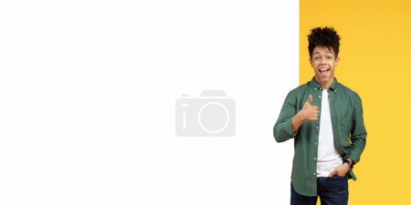 Foto de Sonriente joven negro haciendo gestos con los pulgares hacia arriba con un fondo amarillo y blanco - Imagen libre de derechos