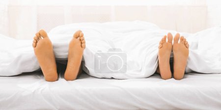 Foto de Pareja cariñosa acostada en la cama, pies desnudos debajo de una manta blanca, espacio libre - Imagen libre de derechos