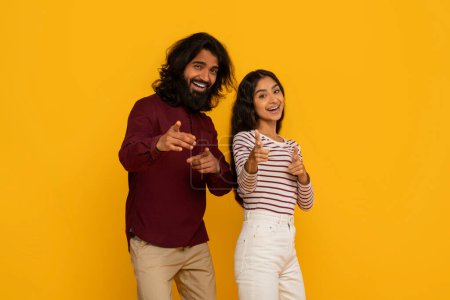 Photo for An engaged couple points directly at the viewer, their animated expressions suggesting an interactive call to action on yellow - Royalty Free Image