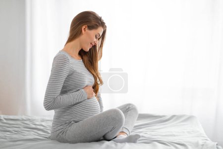 Werdende Mutter sitzt im Bett und spürt die Bewegungen des Babys, was auf das Leben und die Verbundenheit in ihr hinweist