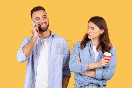 A man talking on the phone while an annoyed woman with a coffee cup looks at him disapprovingly