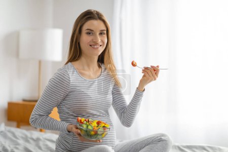 A joyful pregnant woman eats a colorful salad, underscoring the importance of a balanced diet during pregnancy