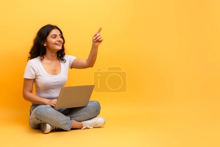 Foto de Una mujer señala hacia arriba mientras está en su computadora portátil, sugiriendo inspiración o descubrimiento durante la interacción digital - Imagen libre de derechos