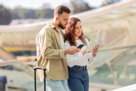 Una joven pareja navega por los viajes con un mapa y un smartphone, incorporando métodos tradicionales y digitales