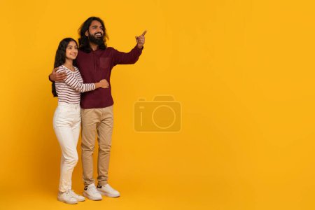 With excited expressions, a man and woman point to something off-frame, invoking curiosity on a yellow background