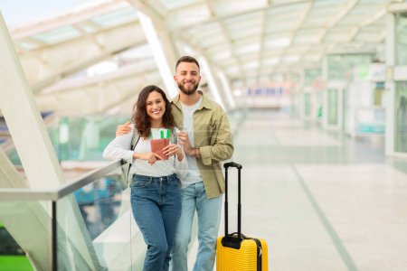 Téléchargez les photos : Joyeux jeune couple montrant des billets ensemble dans un terminal de l'aéroport, exprimant leur excitation au sujet de leur voyage - en image libre de droit