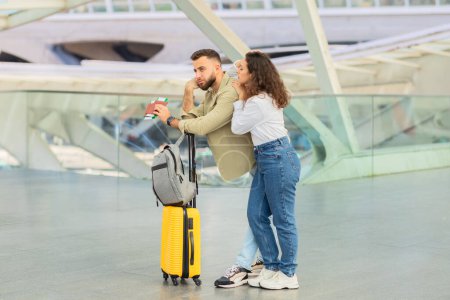 Photo for Upset young couple missed the flight or train, both standing next to a bright yellow suitcase at a modern transit station - Royalty Free Image