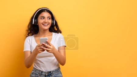 A content young lady interacts with a smartphone while wearing headphones, indicating the digital lifestyle